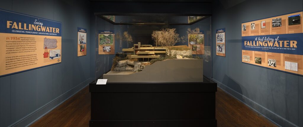A look into the “Seeing Fallingwater – Celebrating Pennsylvania’s Architectural Masterpiece” Exhibit. Model of Fallingwater home at center. Exhibit labels along the outside walls. 